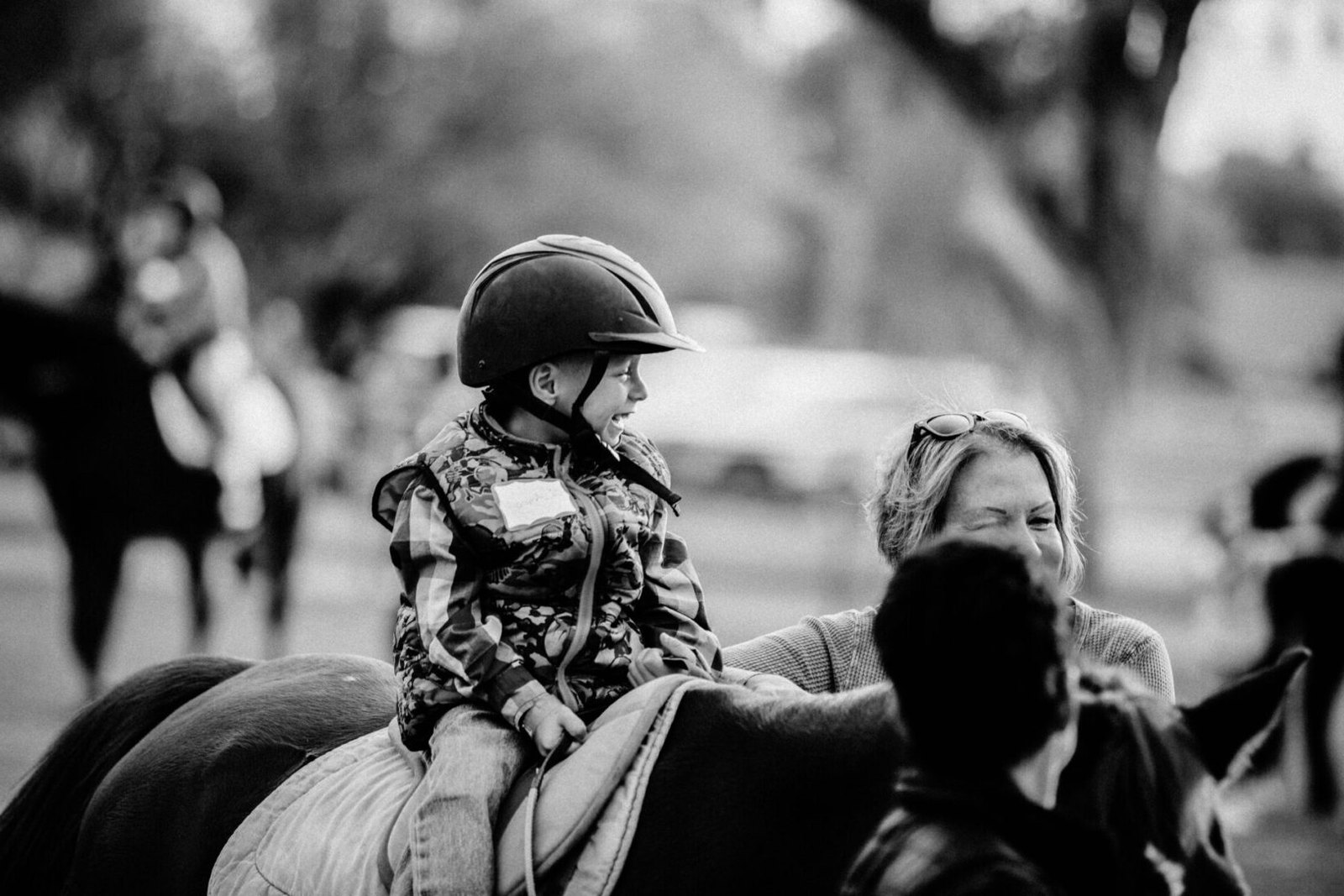 A child smiling while riding a horse with a HŪNKAPI staff member nearby.
